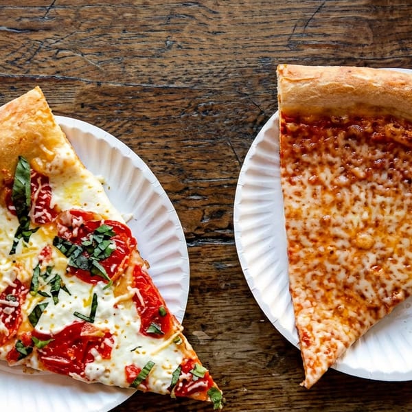 Two pizza slices on paper plates, one Margherita and one cheese, on a wooden table.
